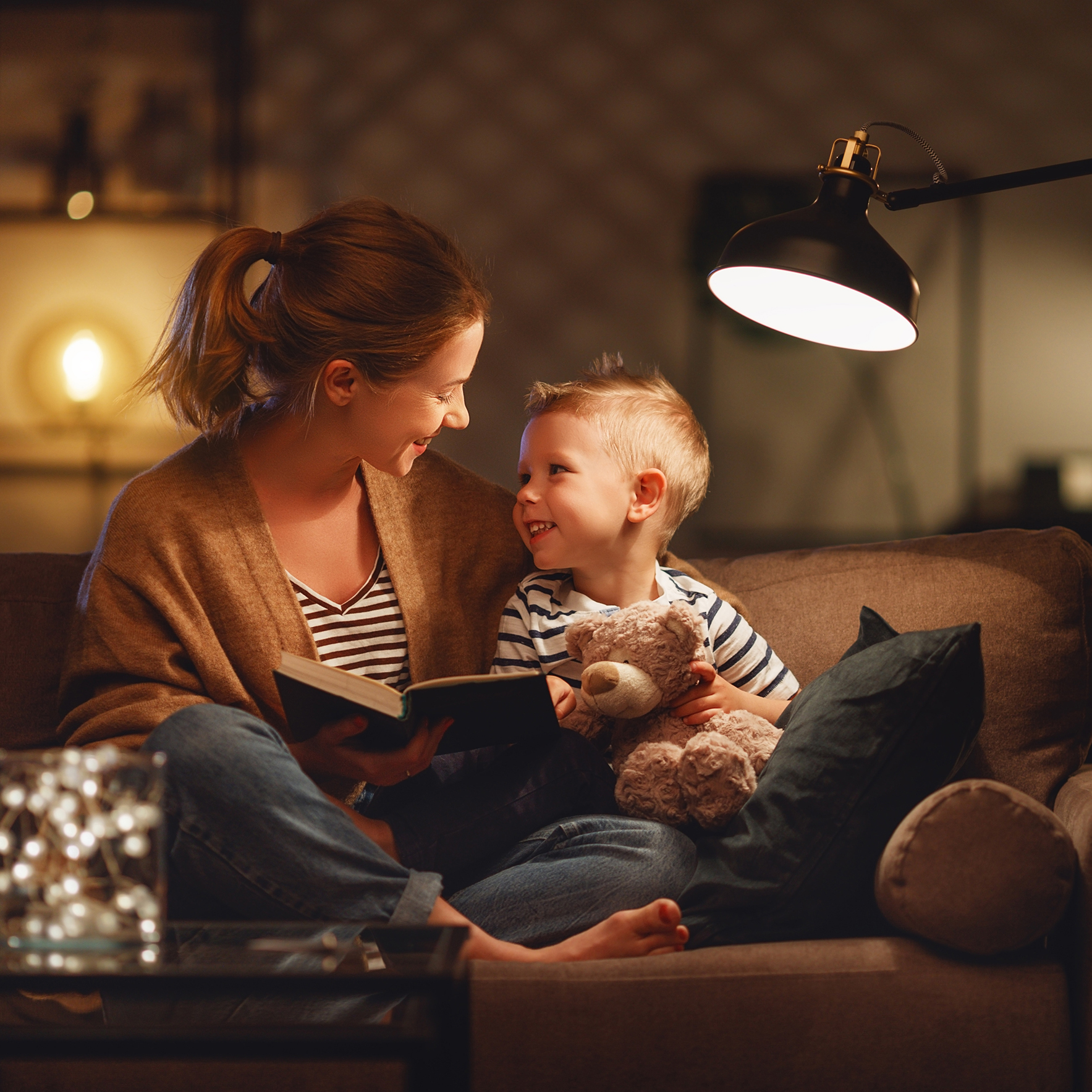 Family before going to bed mother reads to her child son book near a lamp in the evening